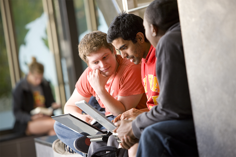 Three guys are looking at the laptop.